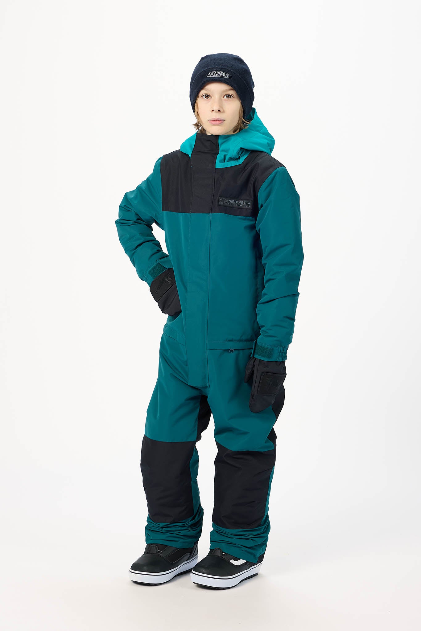 A child modeling a teal and black snowsuit with a matching black beanie, standing against a plain white studio background.
