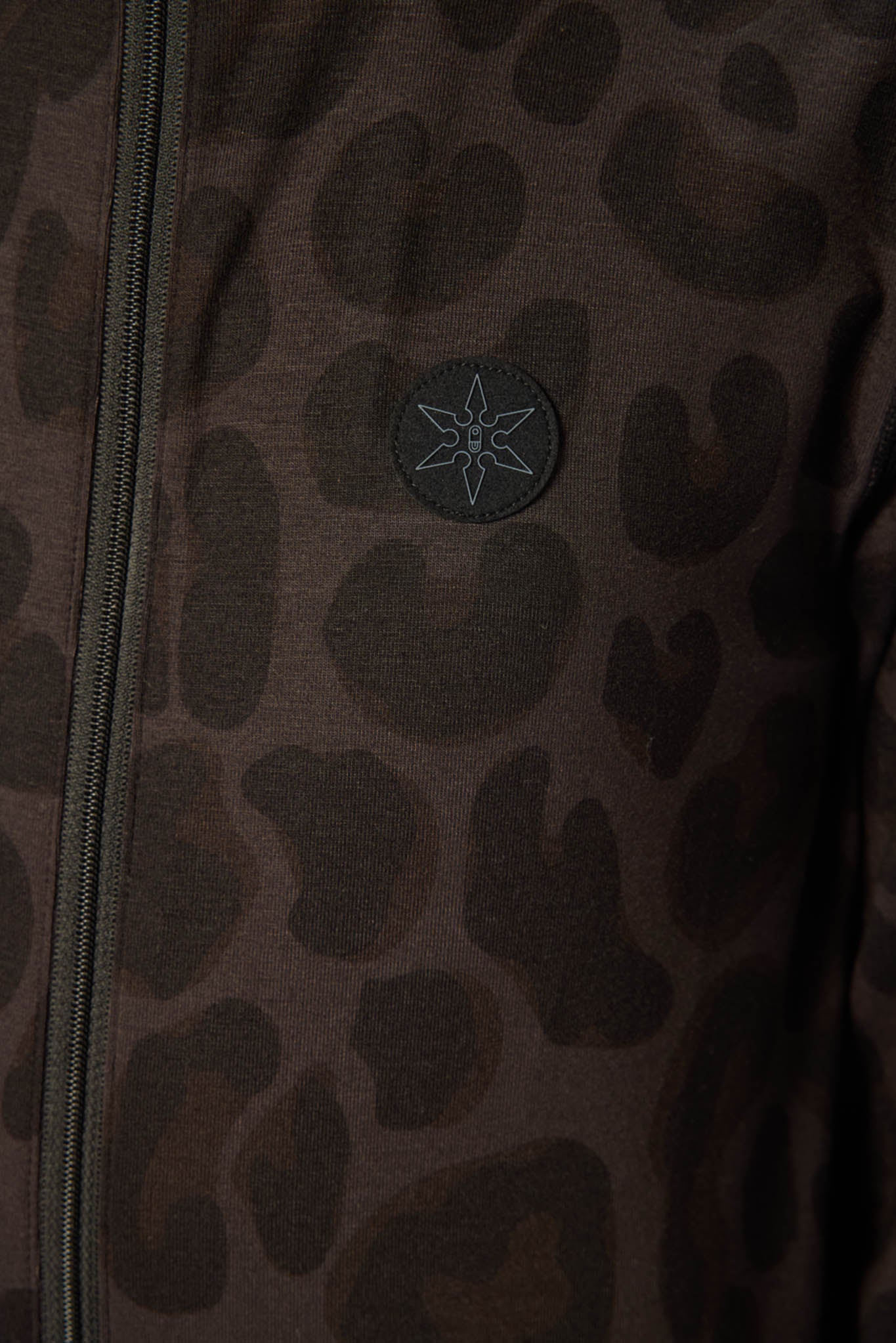 Close-up of a dark brown and black leopard print jacket with a circular embroidered logo on the chest.