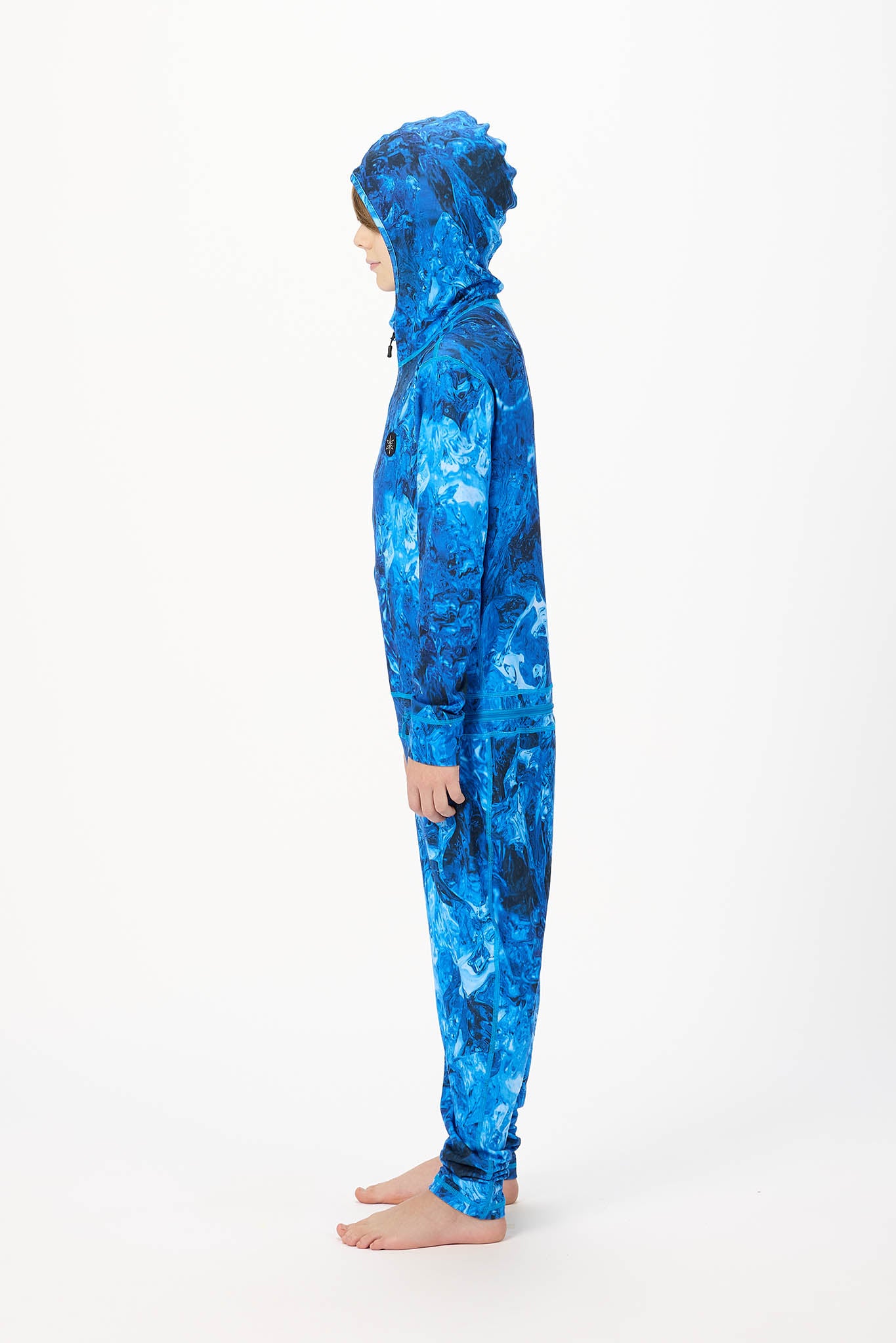 A child wearing a full-body hooded onesie with an abstract blue and black marbled pattern, shown in side profile against a plain white studio background.