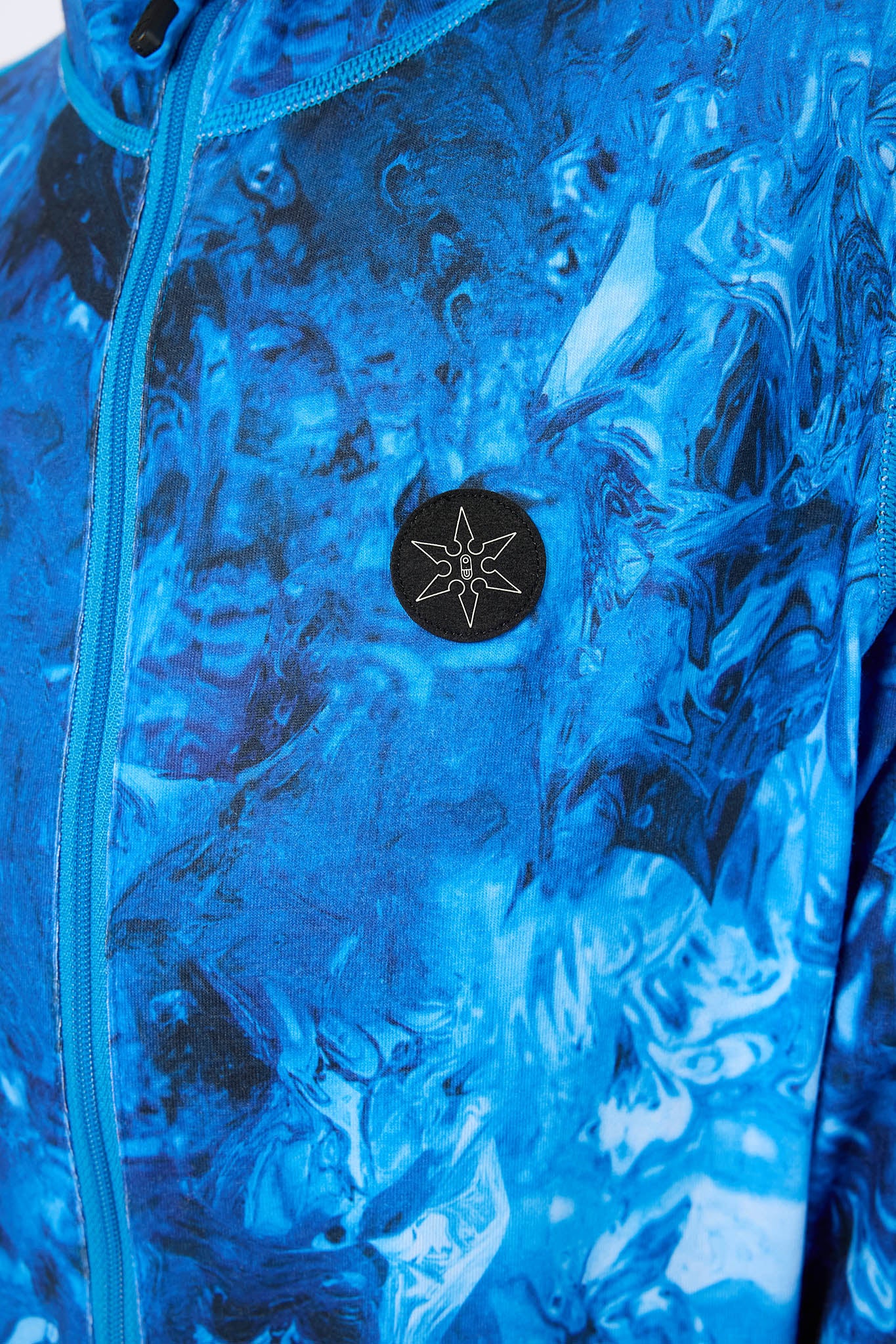 Close-up of a blue marbled patterned jacket with a black circular chest patch featuring a white compass-like symbol.