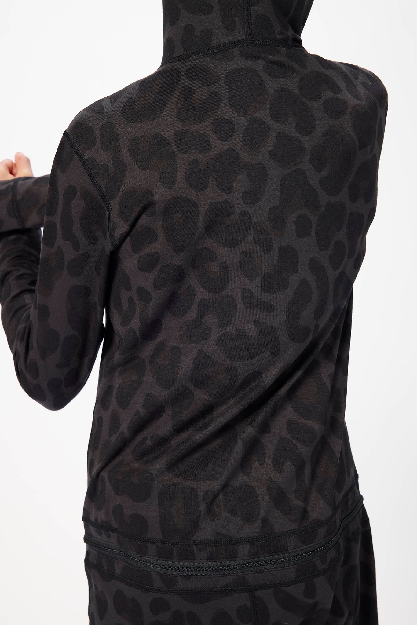 A close-up back view of a person wearing a black long-sleeve top with a dark gray tonal leopard print pattern, paired with matching bottoms against a plain white background.