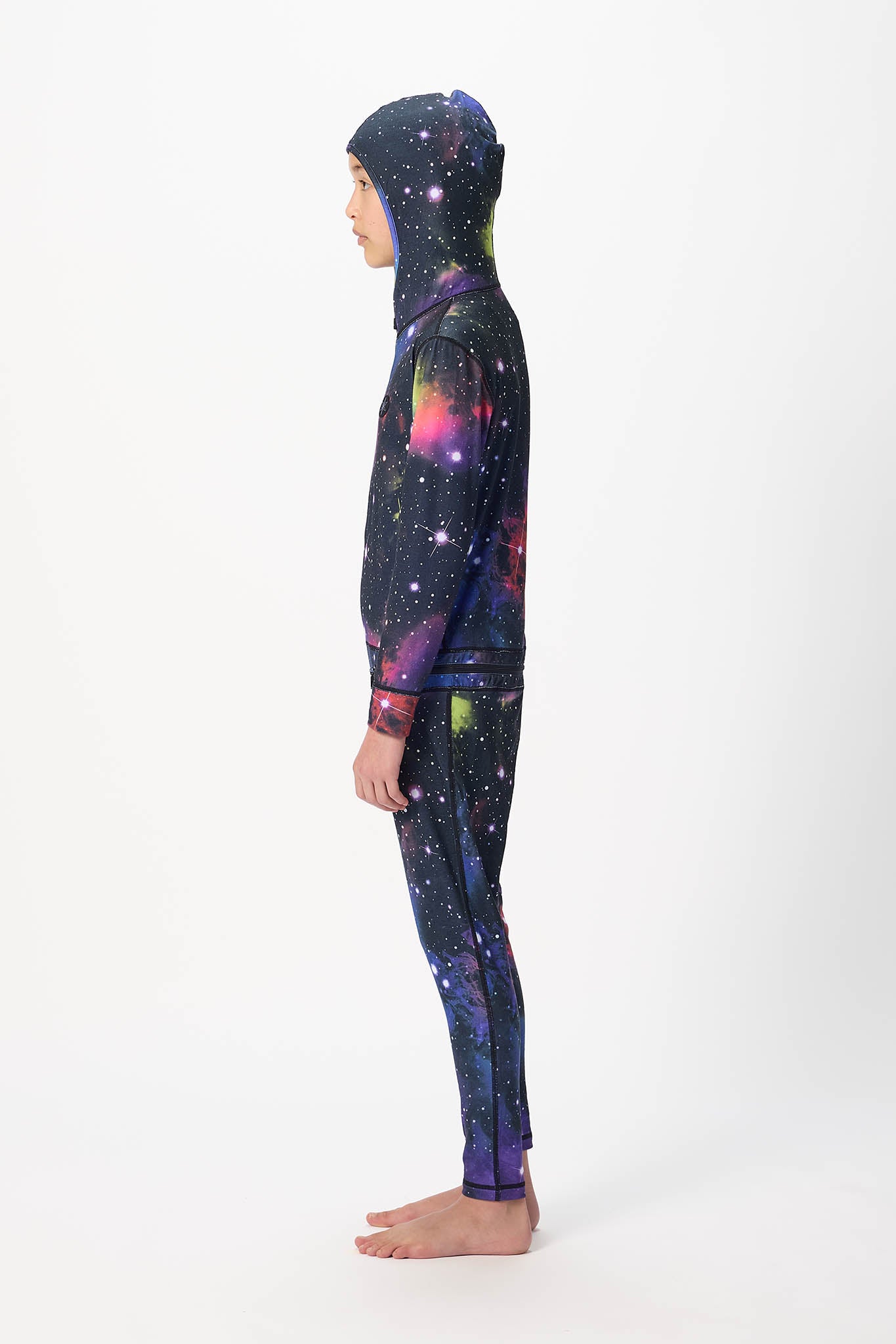 A child model shown in profile wearing a matching hooded sweatshirt and leggings set with a vibrant galaxy print on a plain white studio background.