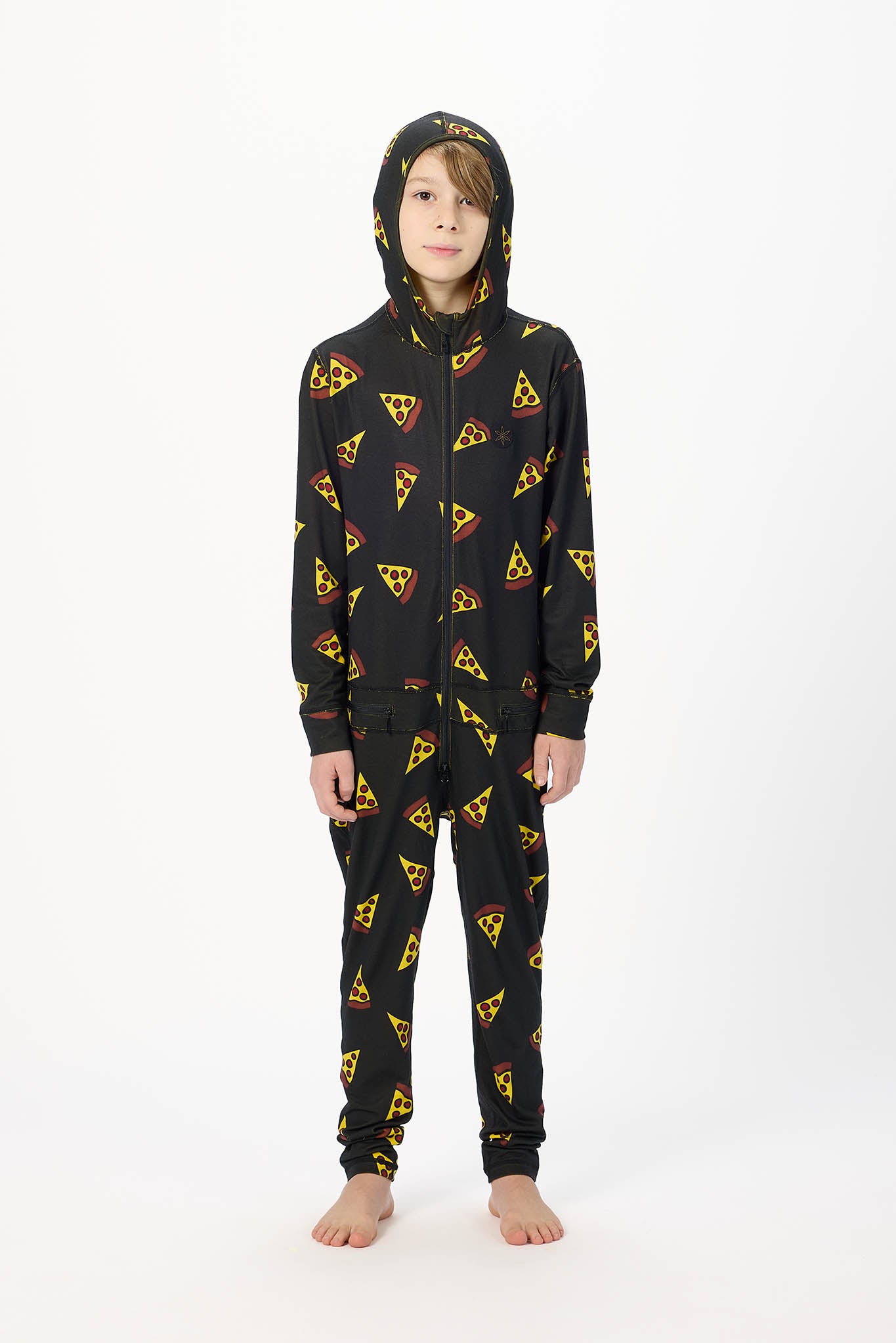 A child wearing a black hooded one-piece pajama or sweatshirt with an allover pizza slice print, standing against a plain white studio background.