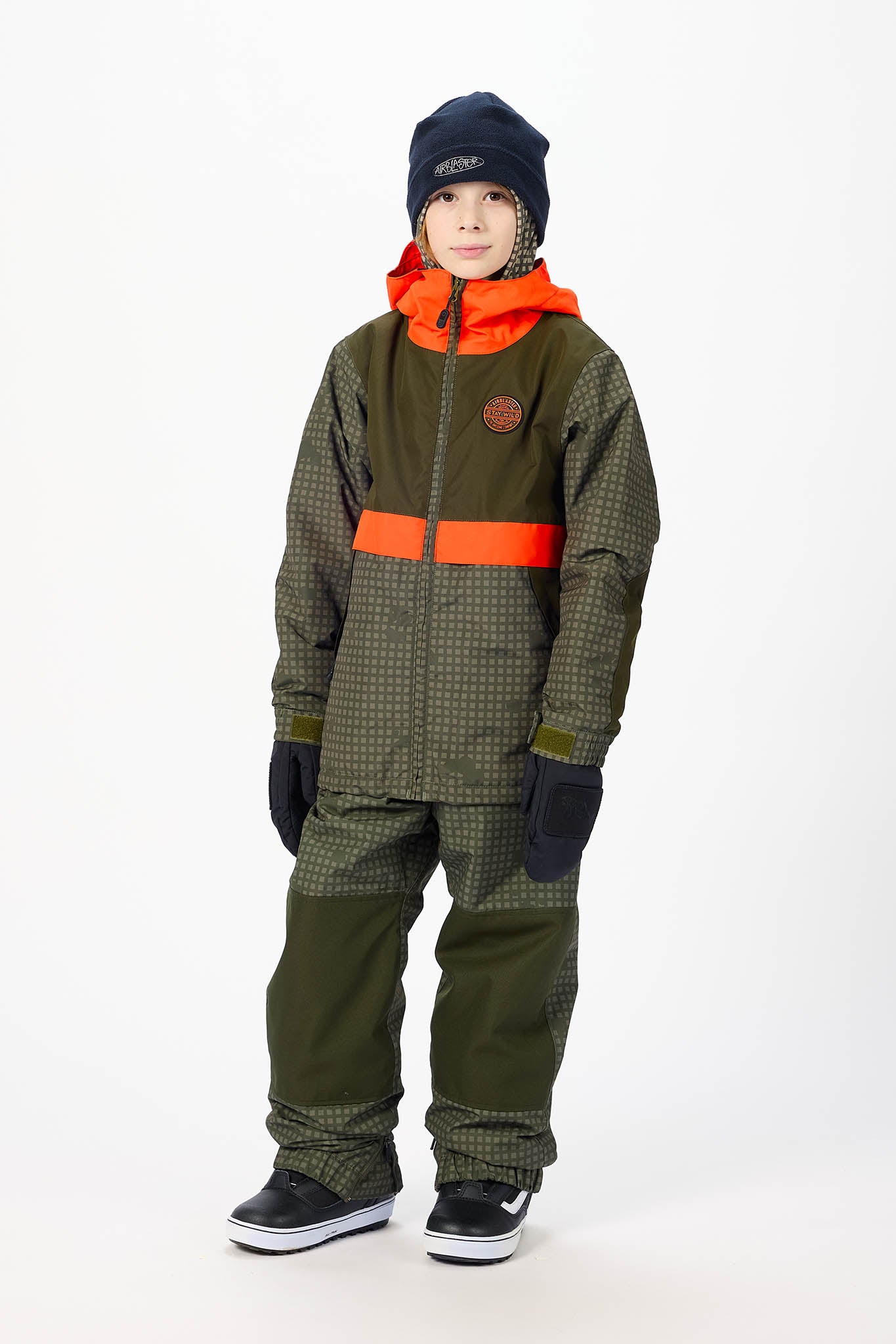 A child wearing a dark green and black patterned snowsuit with bright orange accents, a black beanie, and black gloves, standing against a plain white studio background.