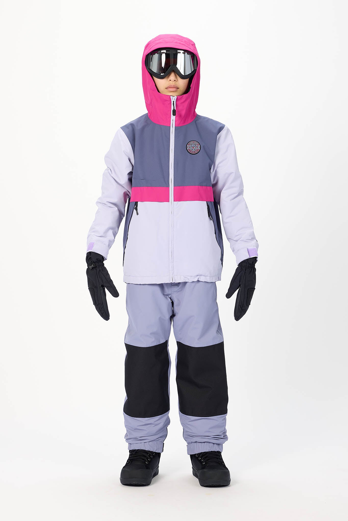 A child modeling a color-blocked ski jacket and matching snow pants in light purple, dark purple, and bright pink, with a pink hood, black gloves, and goggles.
