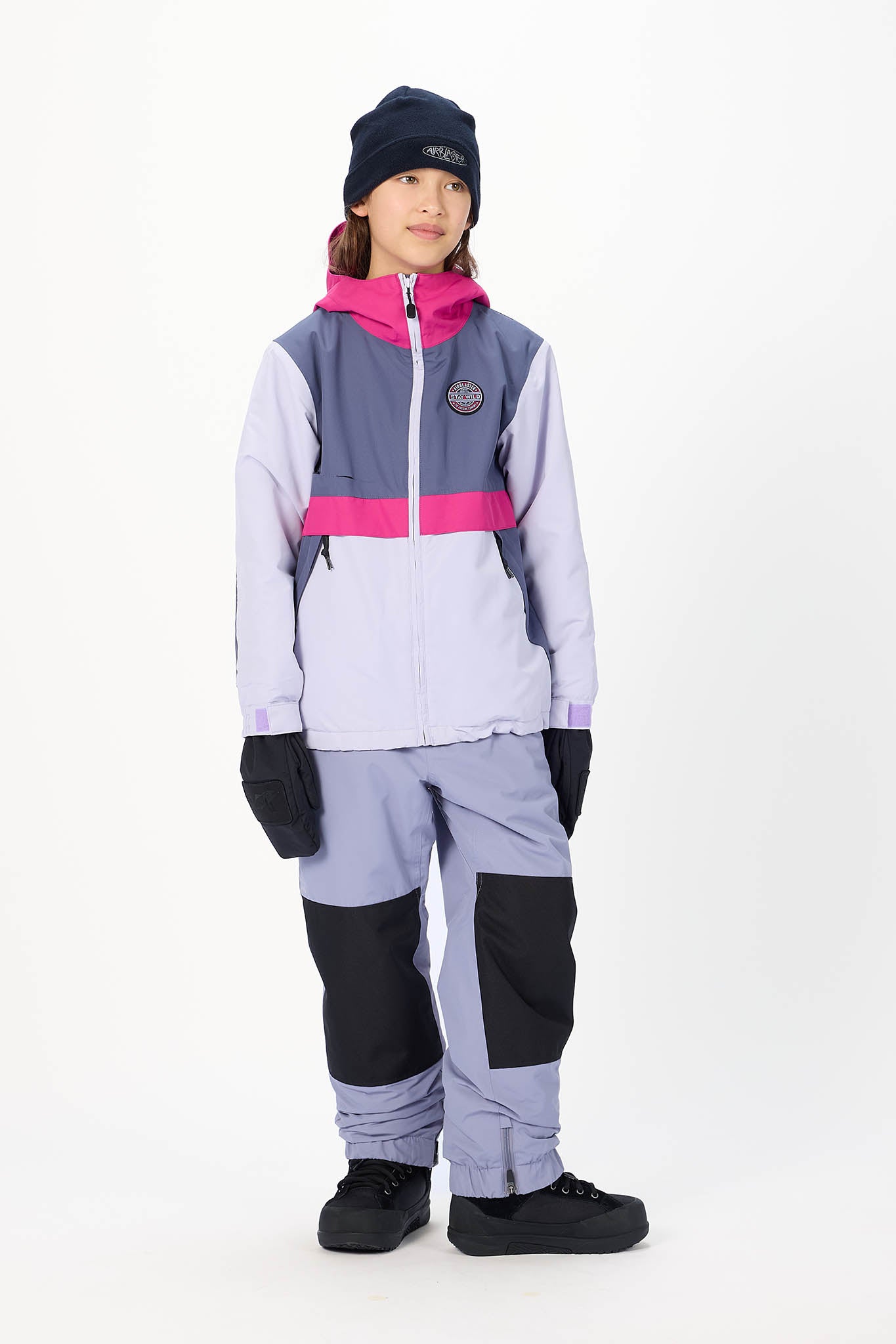 A child model wearing a color-blocked ski jacket, matching pants, black gloves, and a dark navy beanie against a plain white studio background.