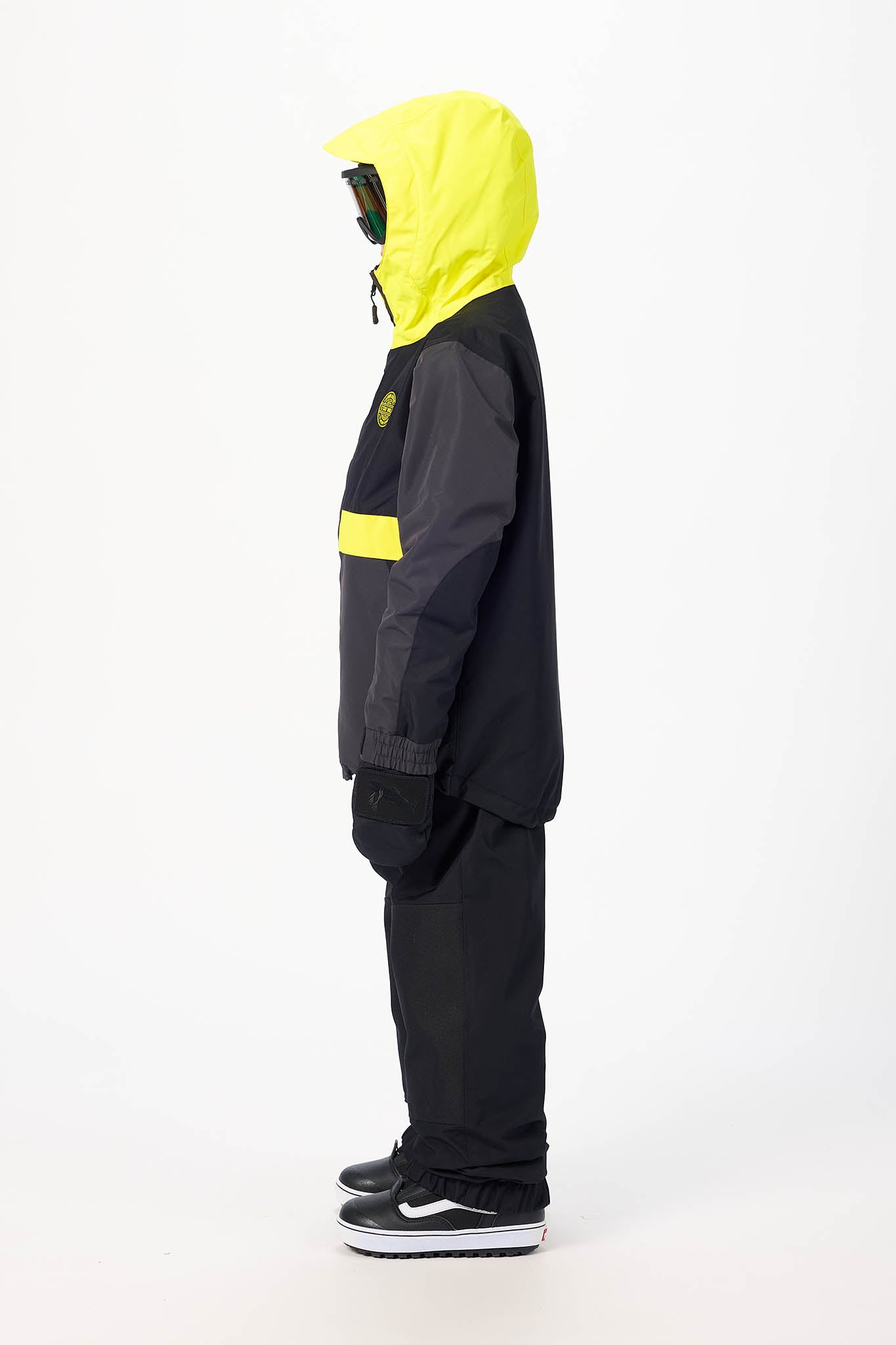 A person shown in profile wearing a black and neon yellow hooded jacket and black pants against a plain white studio background.